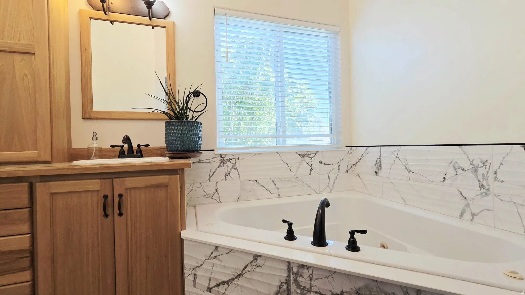 Corner soaking tub with matte black fixtures, surrounded by marble-look tile