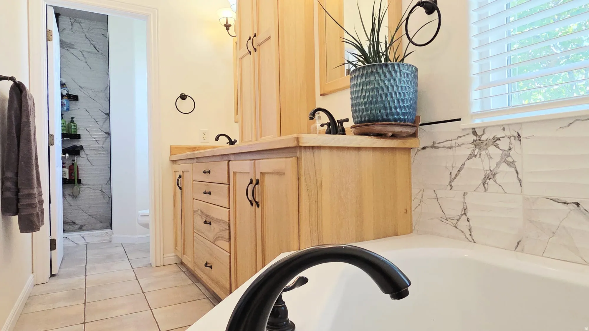 Bathroom featuring a dual vanity with natural wood cabinetry, a built-in bathtub, and marble-look tile accents