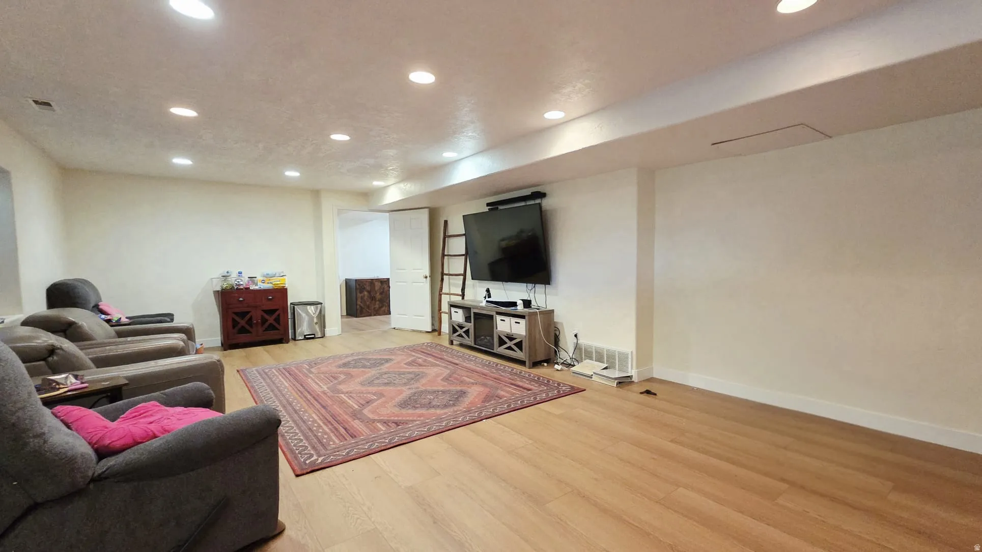 Spacious room featuring light wood-finish flooring, recessed ceiling lighting, and a white baseboard trim