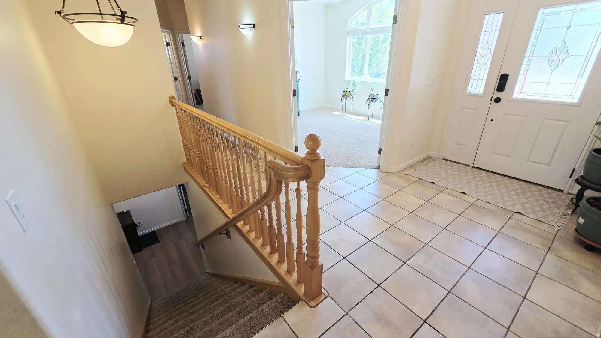 Entryway featuring square tile flooring, a white paneled front door with decorative glass inserts, and a wood railing staircase with carpeted treads