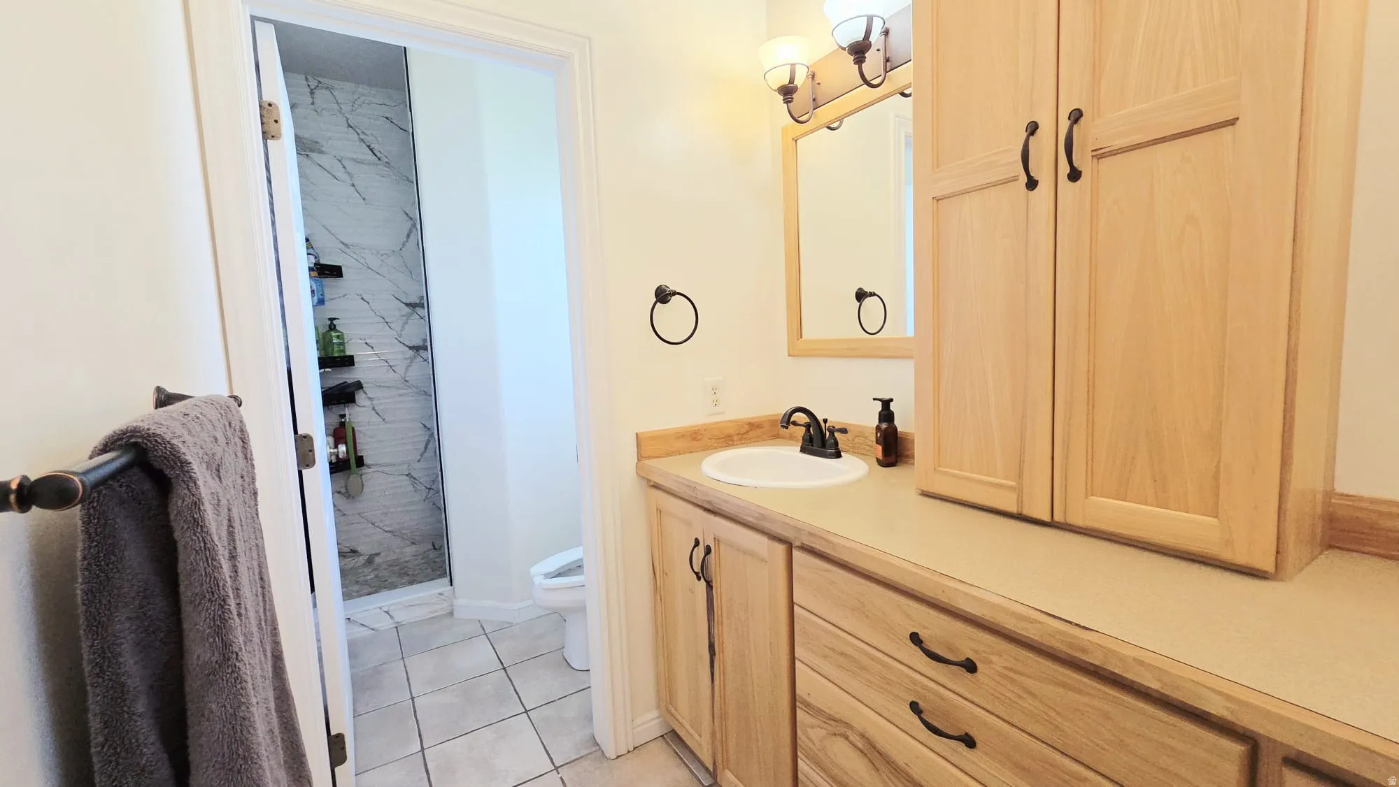 Bathroom vanity with light wood cabinetry, a built-in sink, and a dark bronze faucet