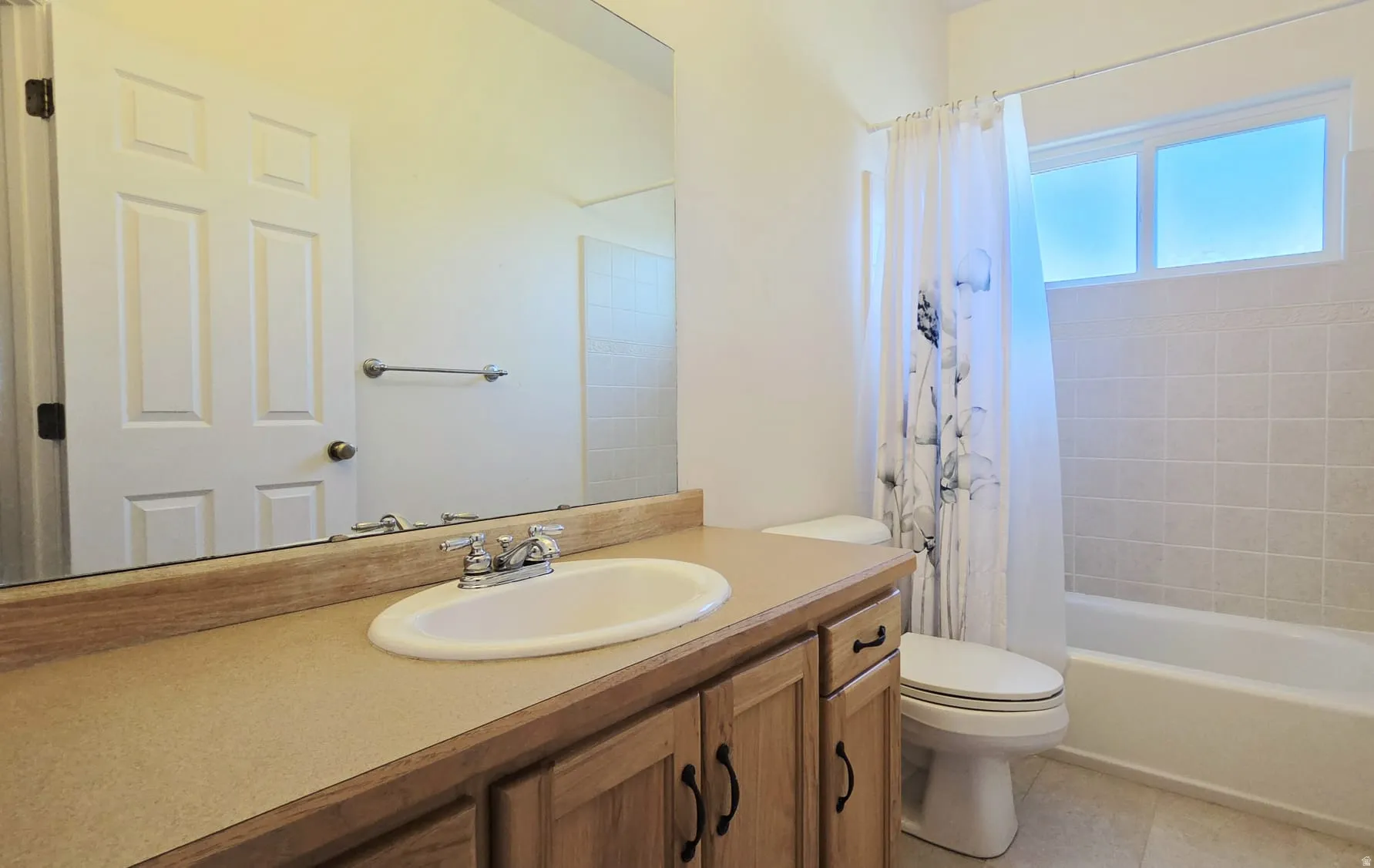 Bathroom featuring a vanity with wood-finish cabinetry, an integrated sink, a large mirror, a toilet, and a bathtub with tiled surround and a frosted window