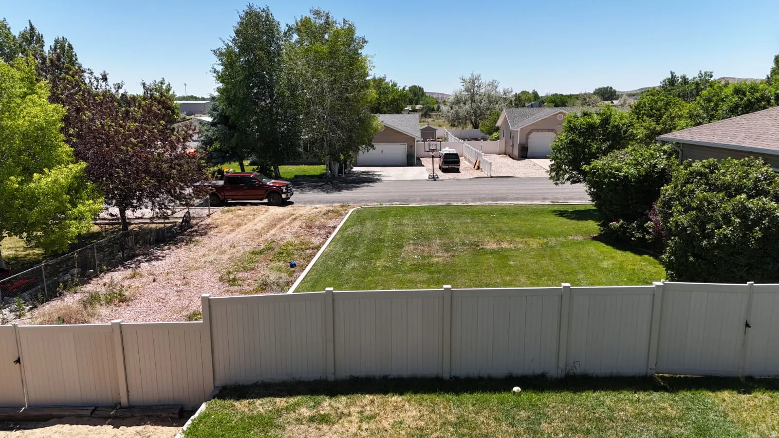 Expansive backyard featuring a manicured lawn, white vinyl fencing, and a gravel area