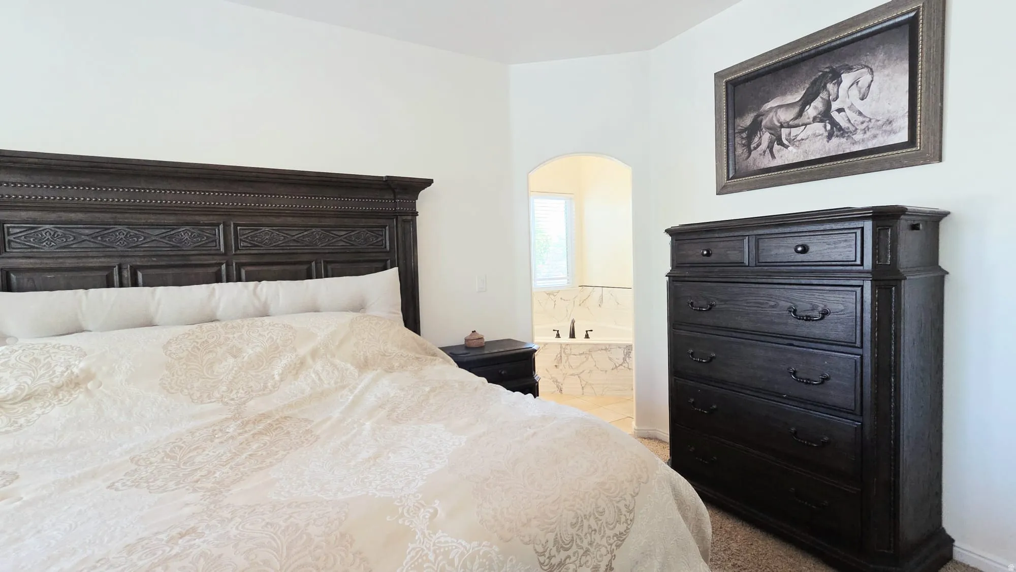 Bedroom featuring a carved dark wood headboard, neutral wall color, and carpeted flooring