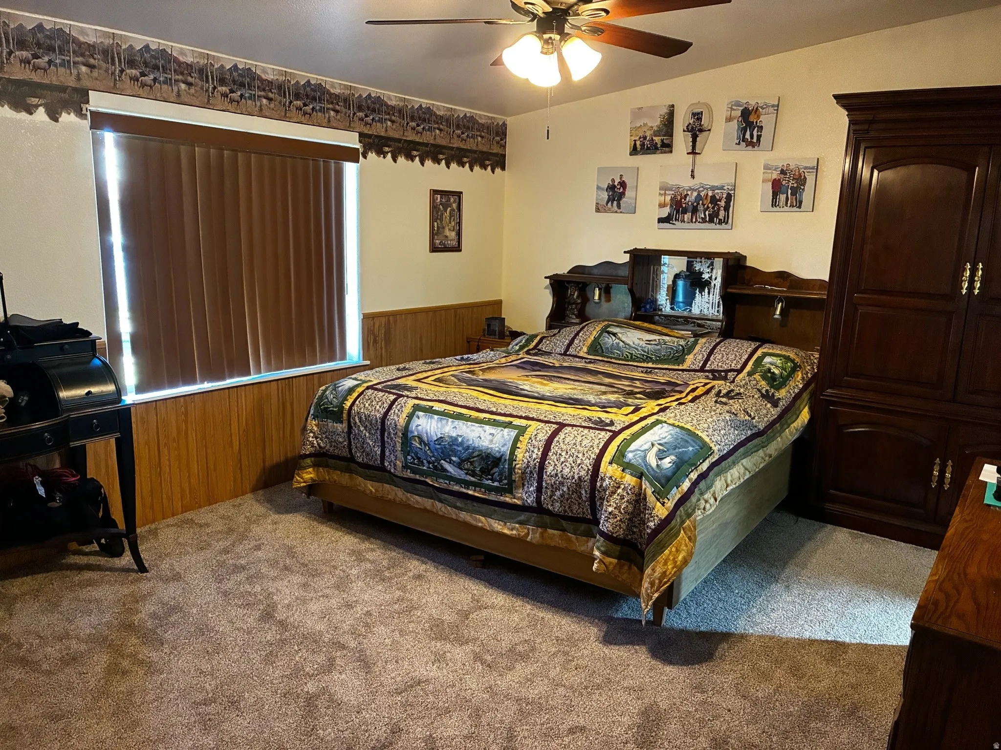 Carpeted room featuring a large window with vertical blinds, wood paneling, and a ceiling fan.