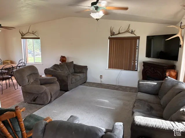 Living area featuring a vaulted ceiling with a ceiling fan, and windows with outdoor views.