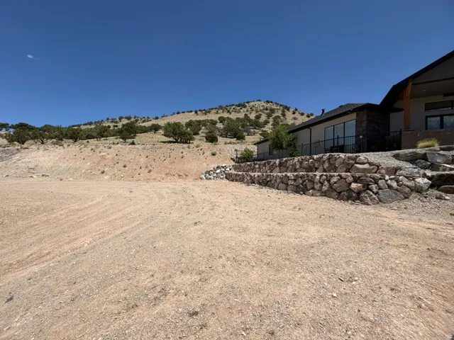 Facing NE.  Expansive graded lot with rock retaining wall, sidewalk access and hillside terrain