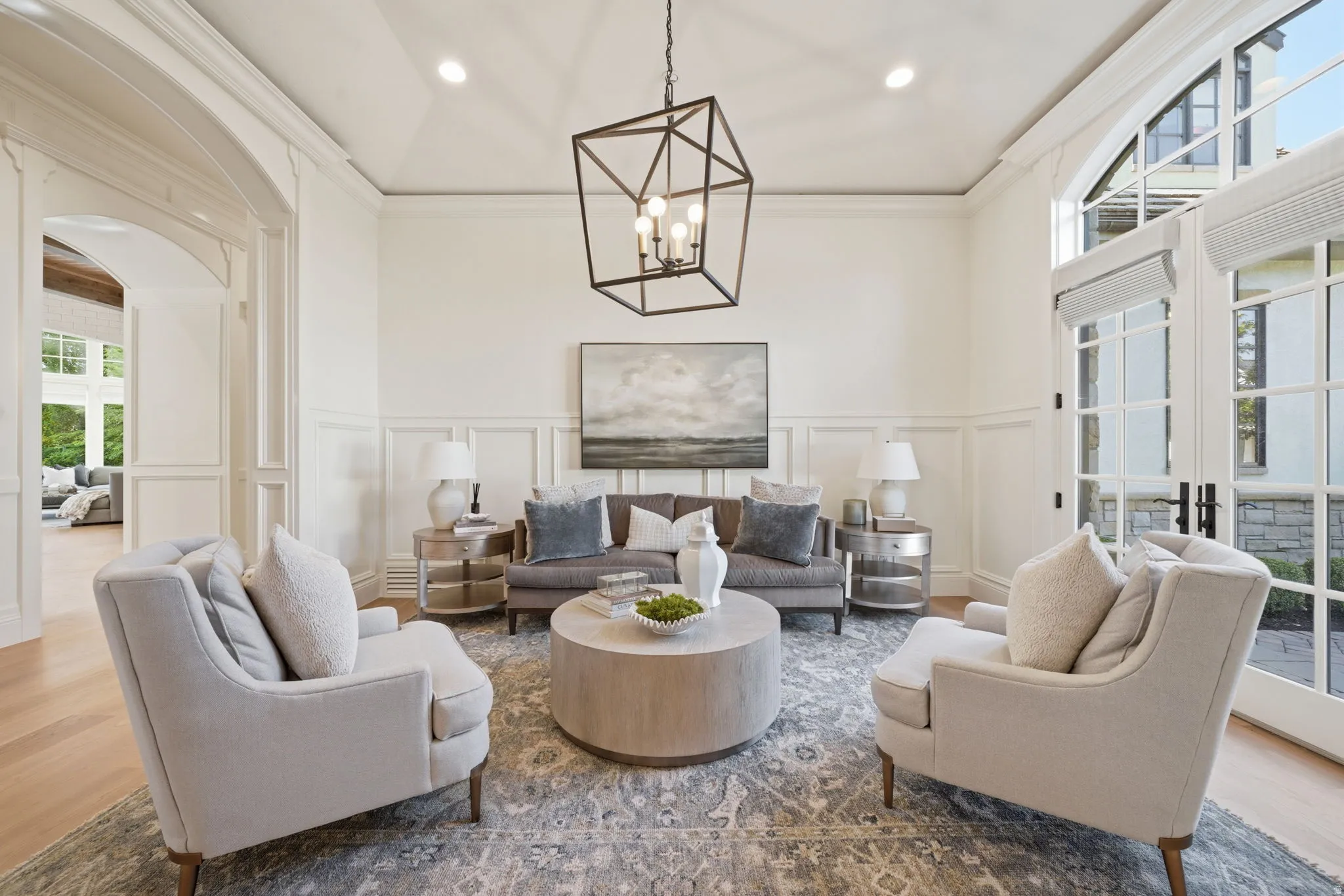 Living area featuring wood-finish flooring, wainscoting, an arched doorway, and double French doors with transom windows