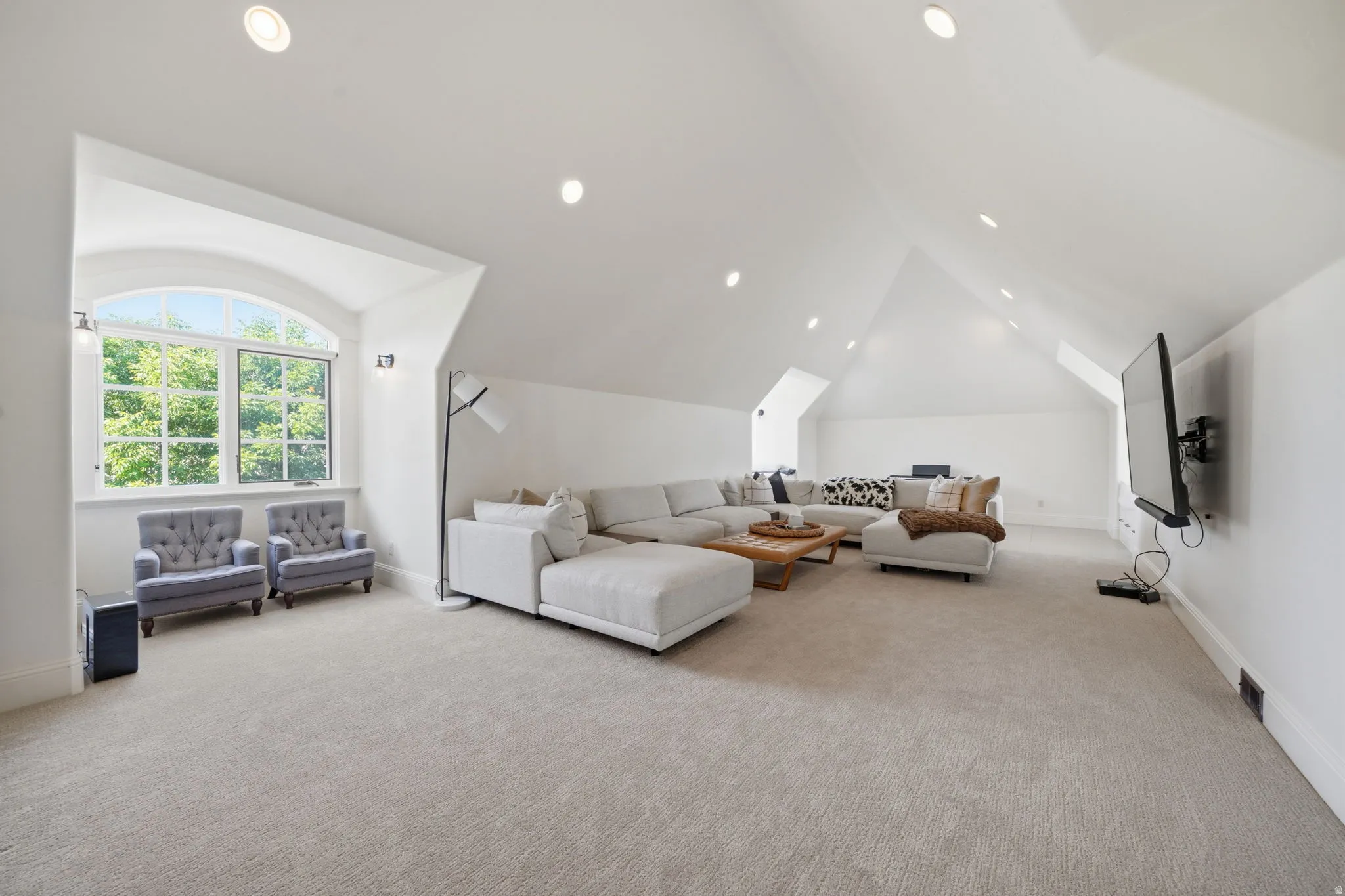 Expansive bonus room featuring vaulted ceilings, recessed lighting, and a broad arched window