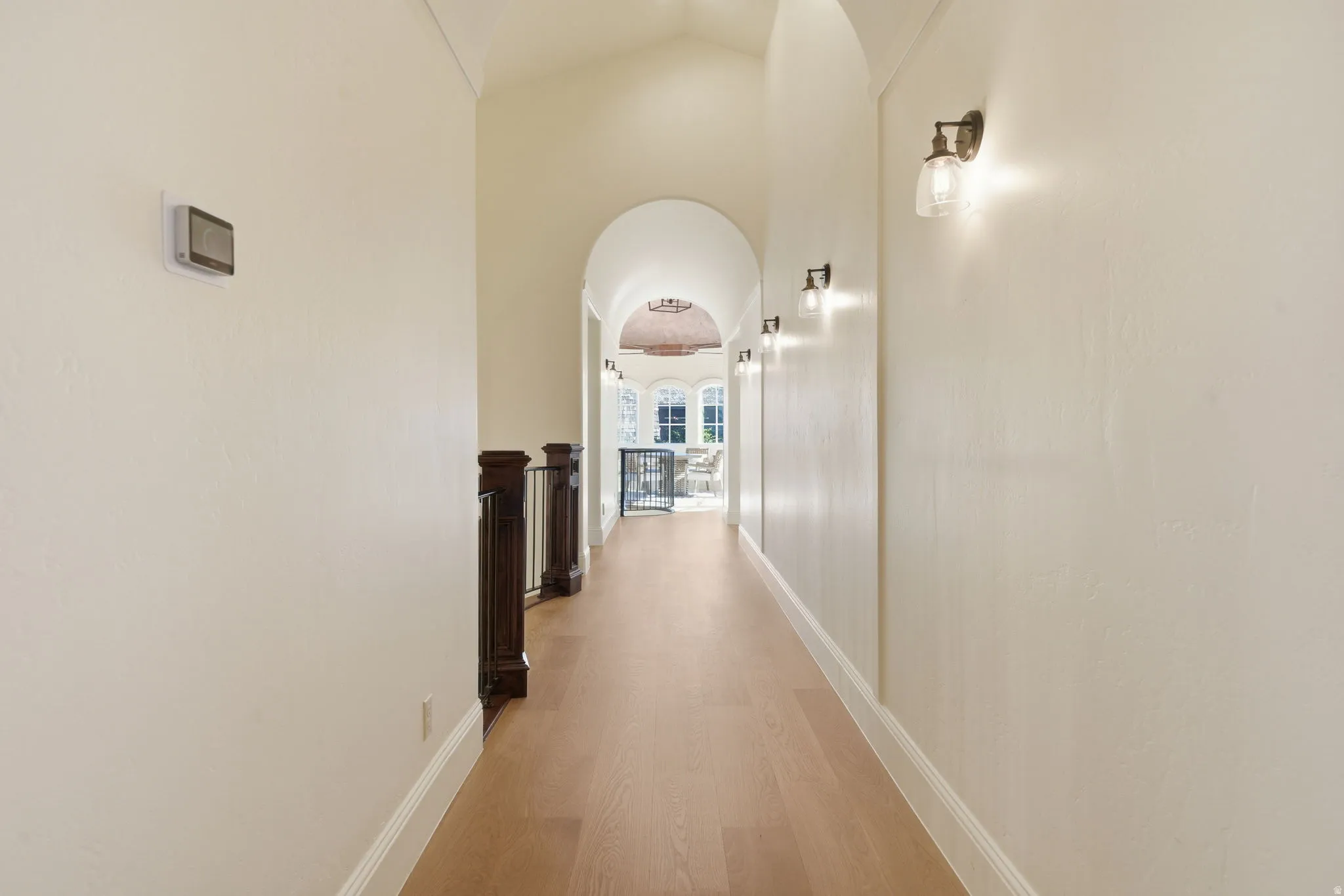 Hallway featuring wood-finish flooring, archways, dark wood balusters, wall sconces, and a wall-mounted thermostat