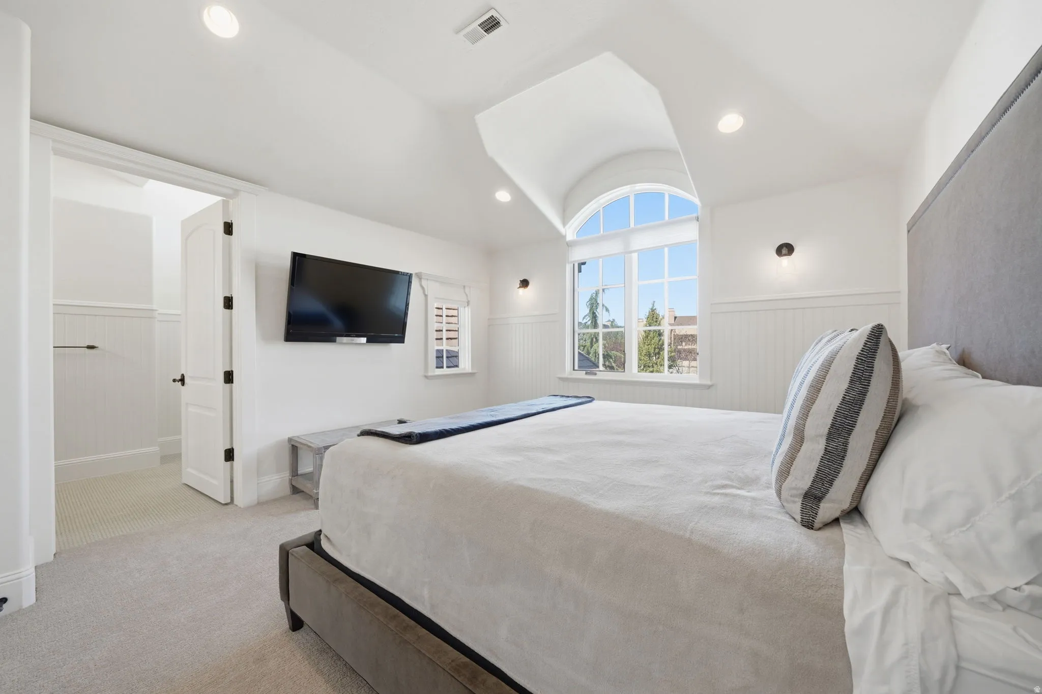 Bright room featuring an arched window, white paneled wainscoting, recessed lighting, and wall-mounted sconces