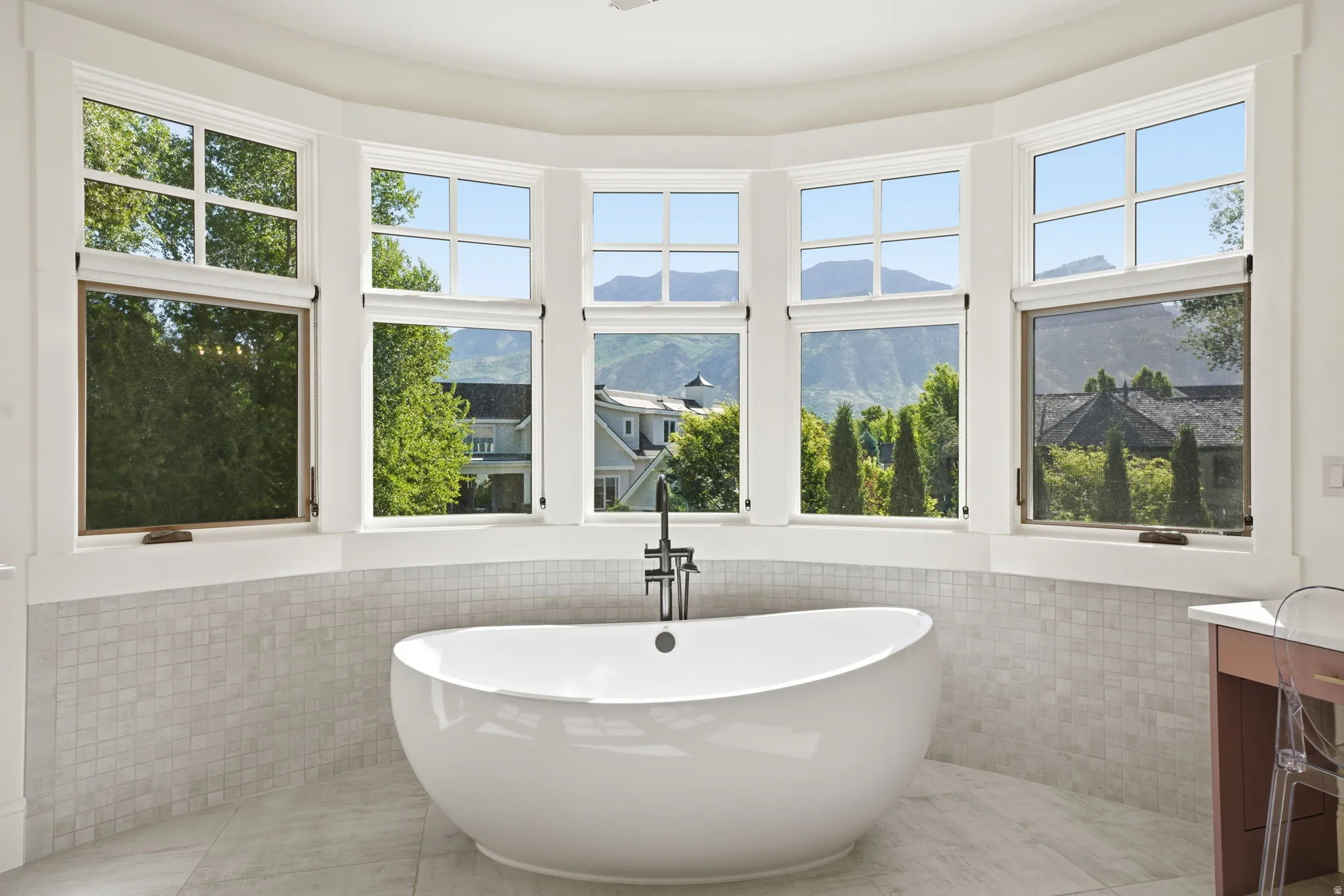 Freestanding soaking tub set against a curved window wall with mountain scenery