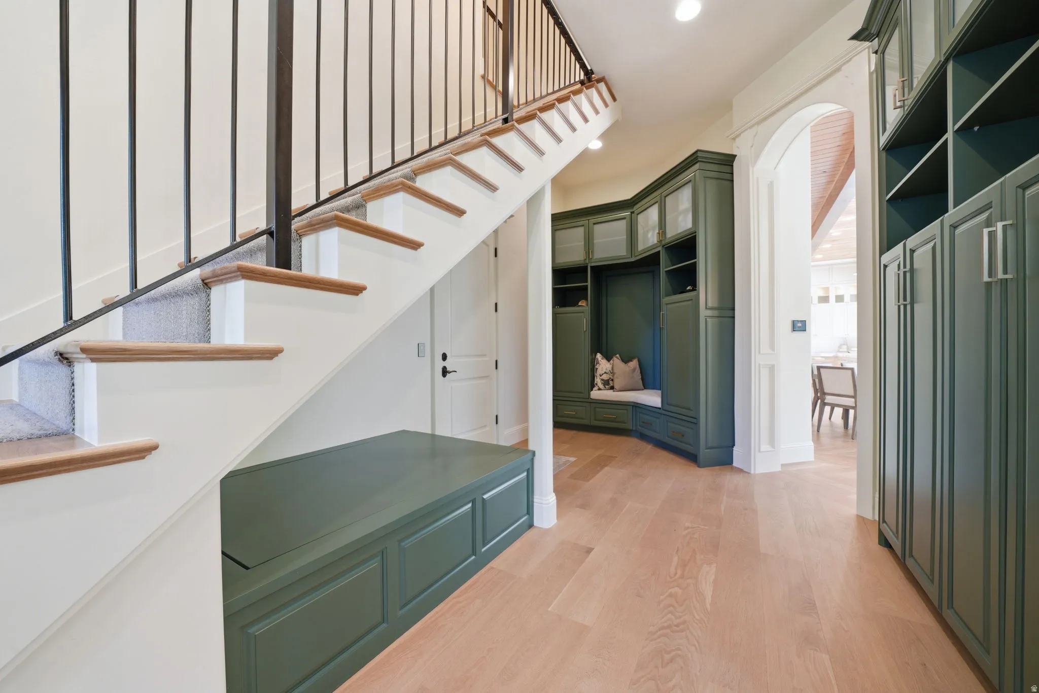 Entryway featuring light wood-finish flooring and a staircase with light carpet treads and a black metal railing