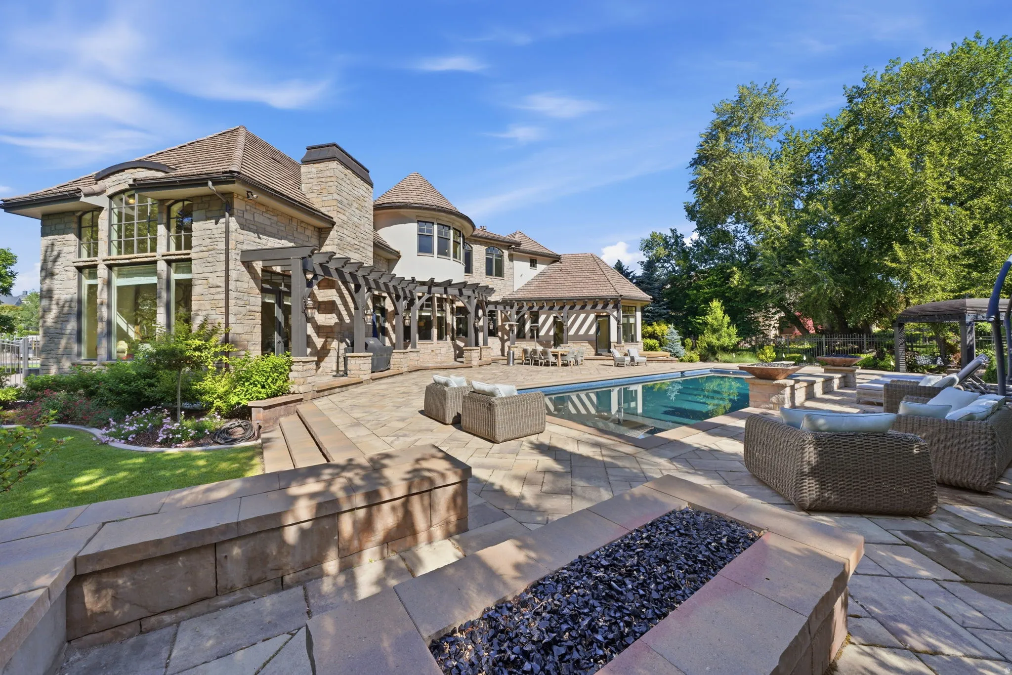Expansive stone patio featuring a built-in fire pit, swimming pool, and pergola-covered dining area