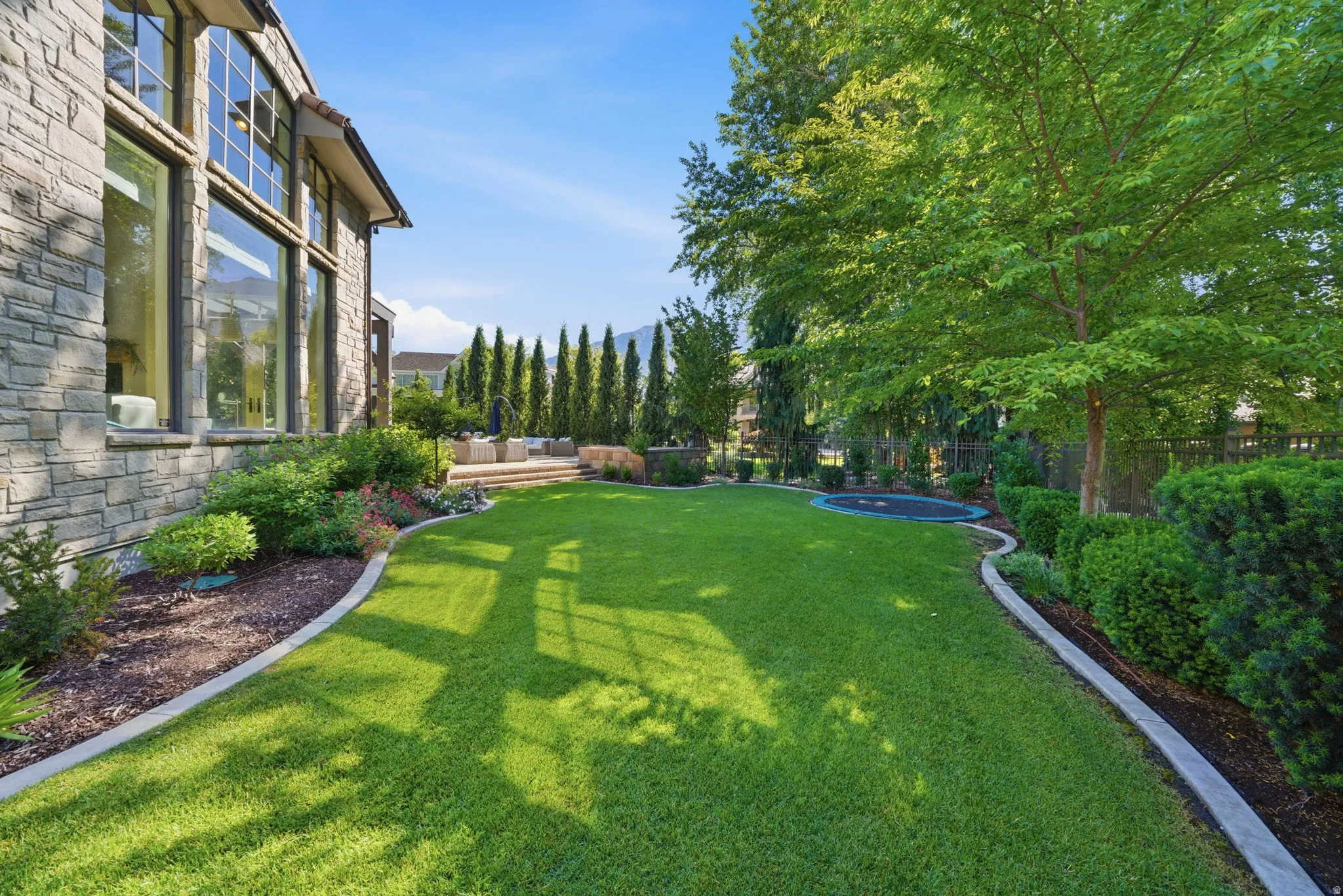 Expansive manicured lawn with concrete curbing, bordered by mature trees and shrubs