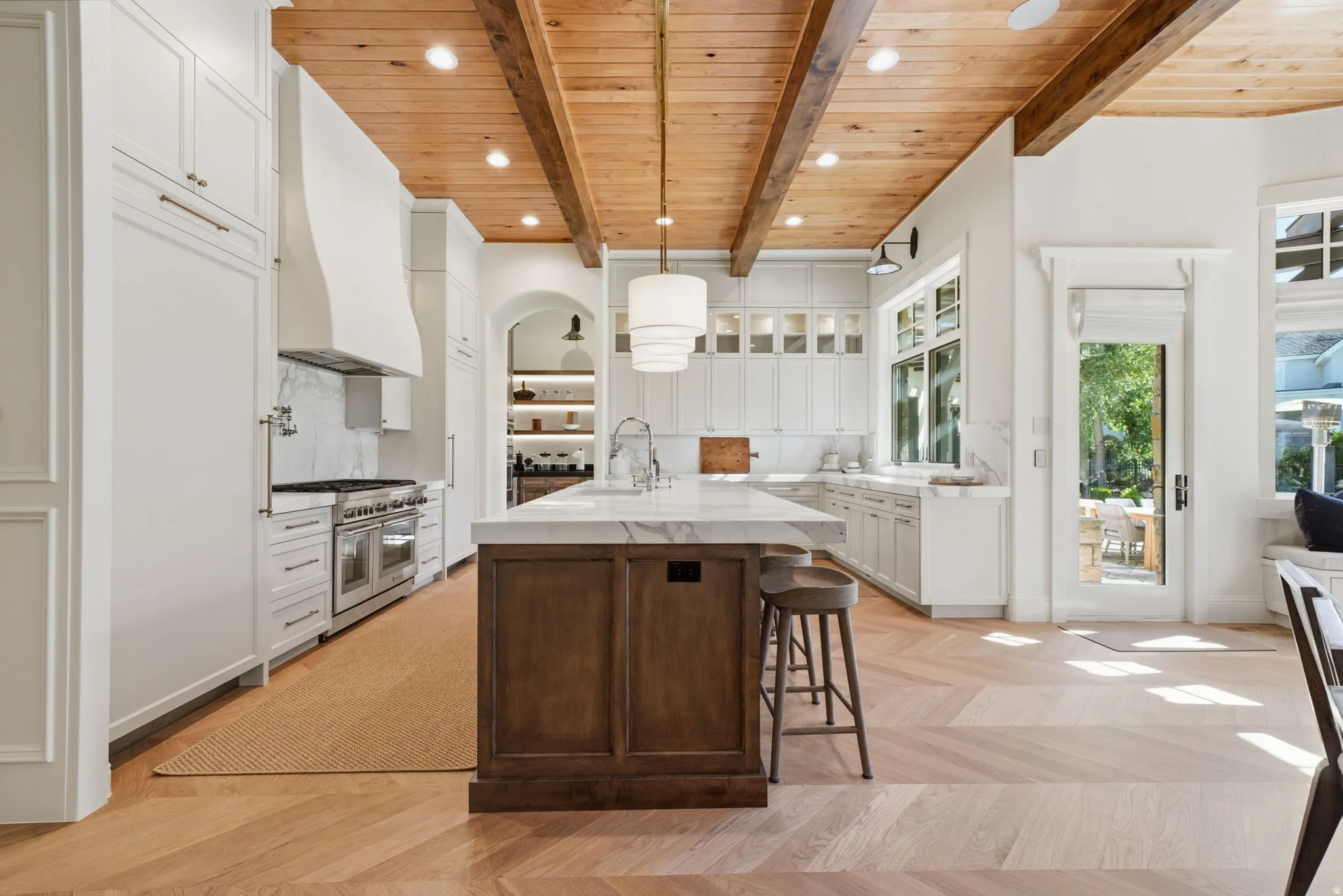 Kitchen with wood-finish beamed ceiling, white cabinetry, a large central island with seating, a stainless steel range, and herringbone wood-finish flooring