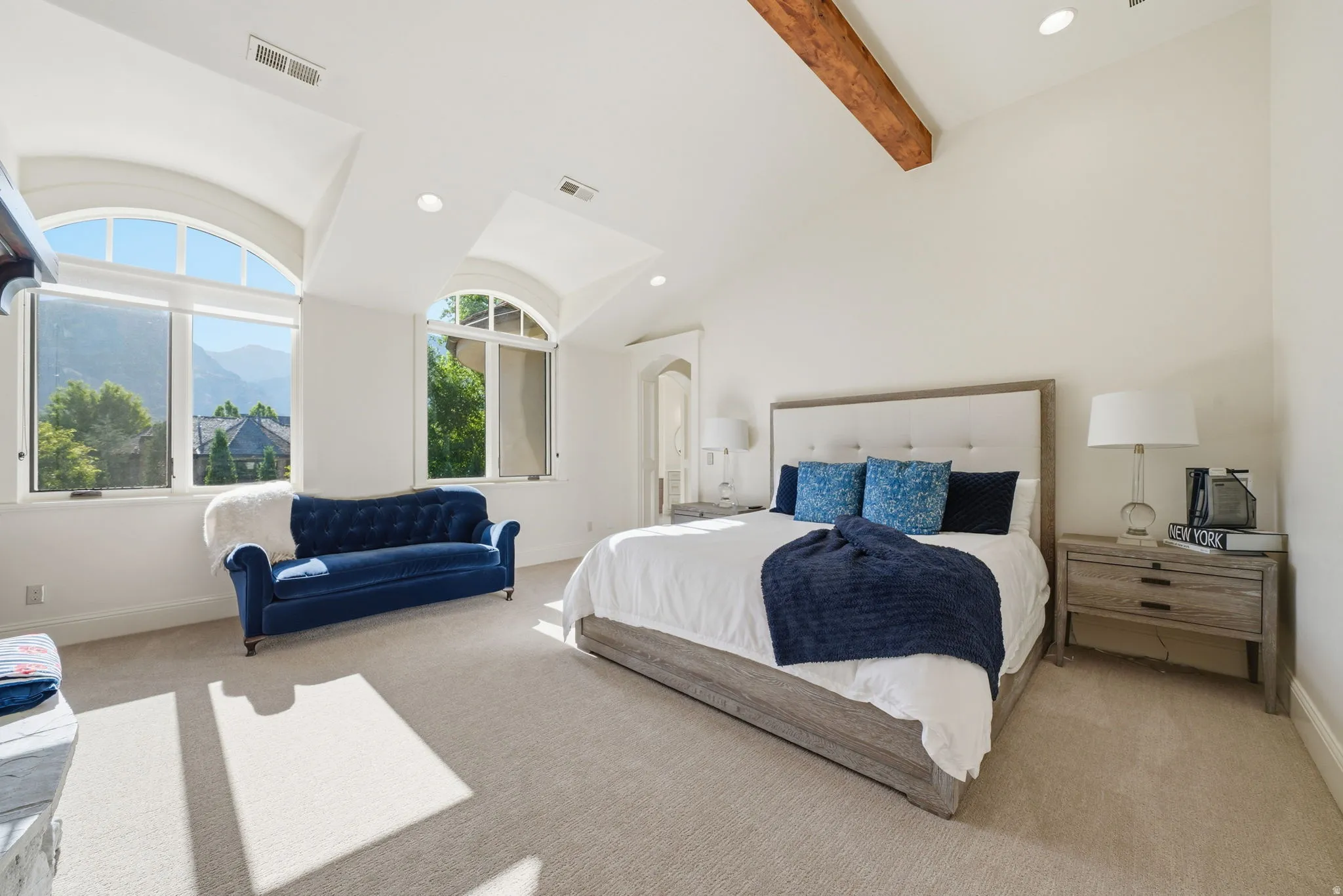 Spacious room featuring vaulted ceilings with a prominent exposed wood beam, recessed lighting, and light neutral carpet