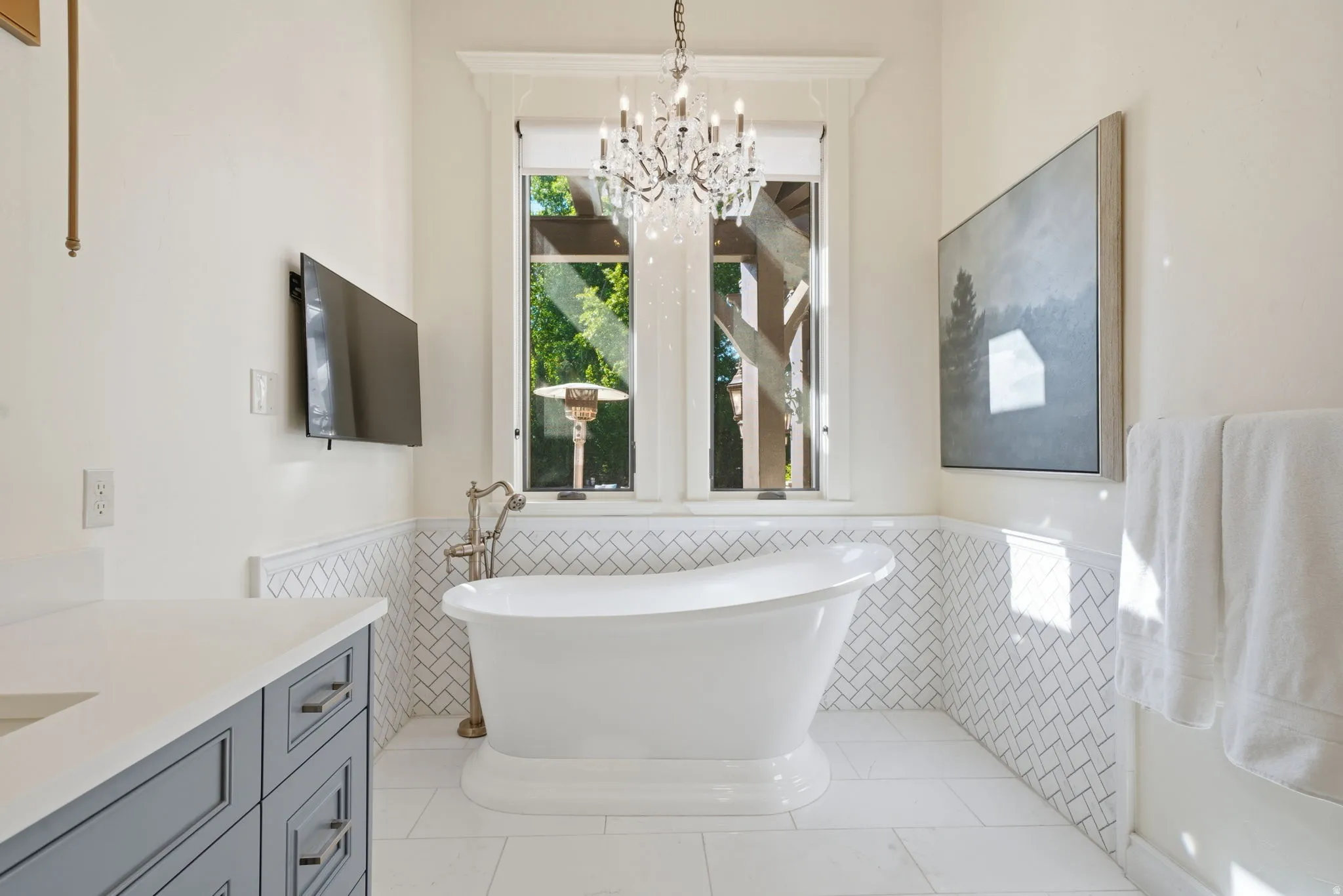 Freestanding pedestal bathtub with floor-mounted fixtures, set against a backdrop of white herringbone tile wainscoting