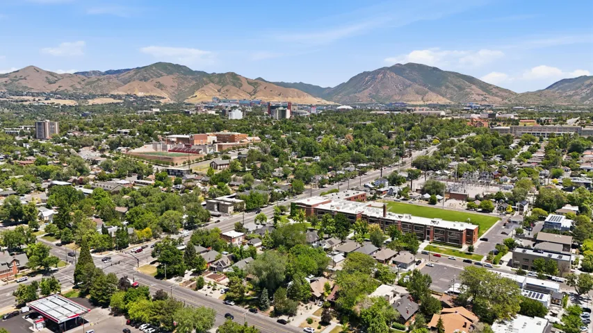 Expansive urban landscape featuring a mix of residential and commercial structures, mature green trees, and paved roadways