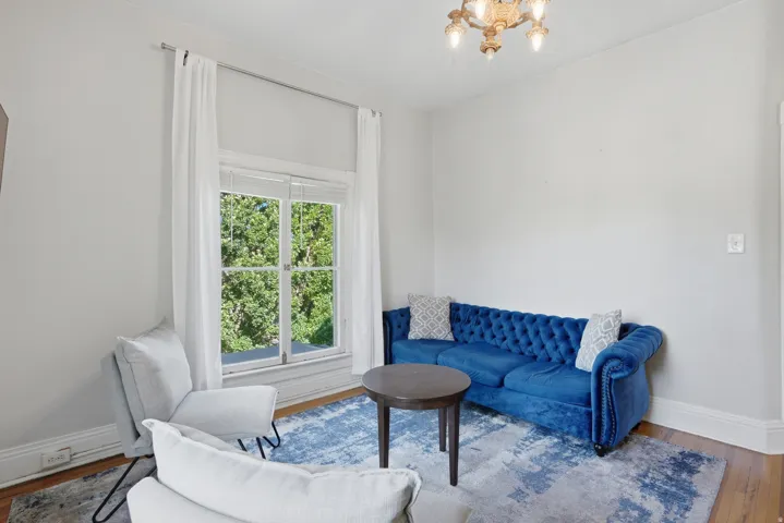Hardwood flooring complemented by white baseboards, a large double window with white trim, and an ornate ceiling fixture