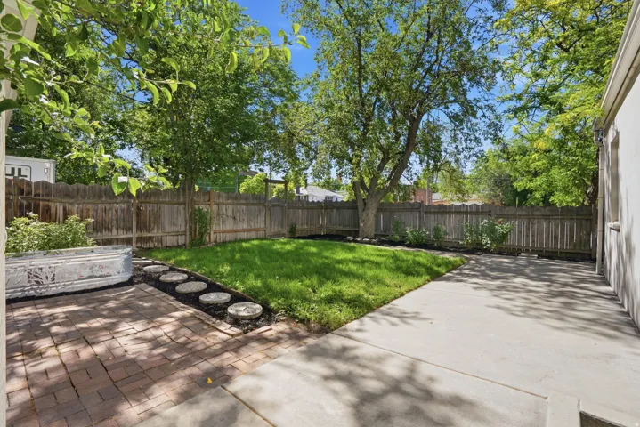Private backyard featuring a concrete patio, a brick-paved patio, a manicured lawn, mature trees, and a wood privacy fence
