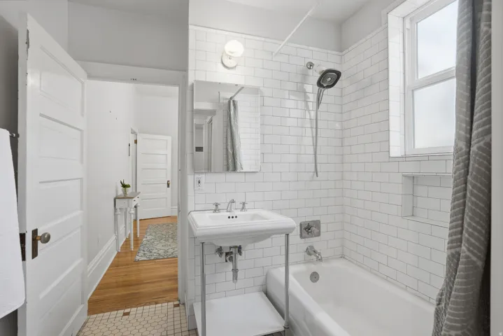 Bathroom featuring white subway tile surround, a pedestal sink with chrome fixtures, and a classic white bathtub