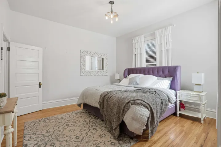 Bedroom featuring wood-finish flooring, white trim, and a window with blinds and ruffled white curtains
