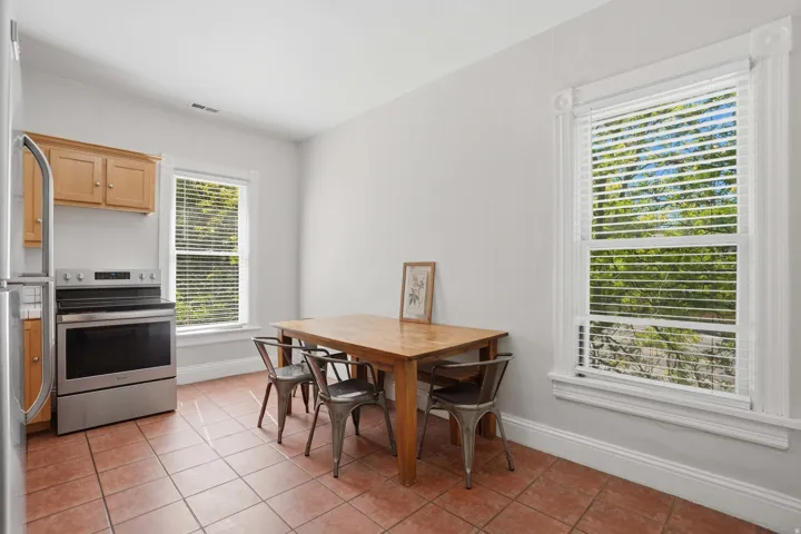 Dining area featuring terracotta-style floor tiles, two large windows with ornate trim, and light-toned wall paint