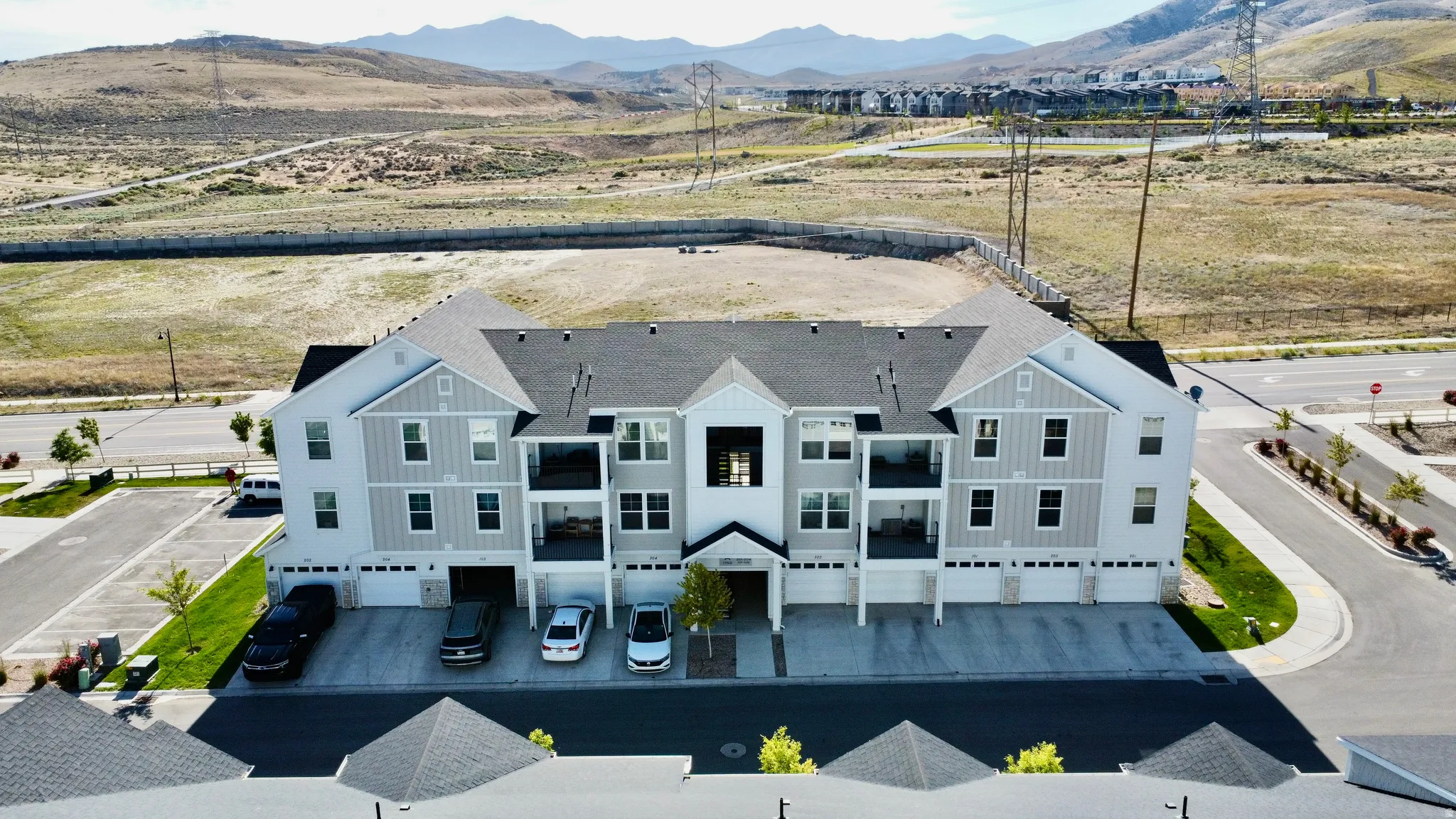 Contemporary multi-level townhome building featuring a grey and white exterior, multiple balconies, individual garage access, and a paved street frontage
