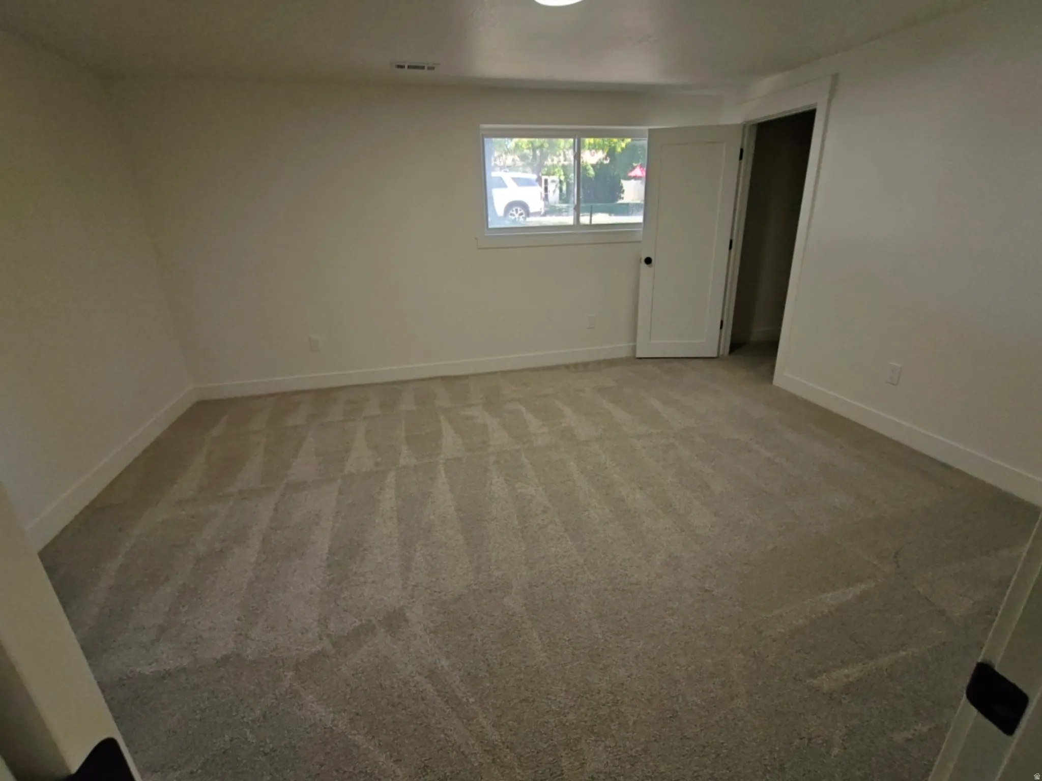 Spacious room featuring new carpeting, white baseboards, and a window with natural light