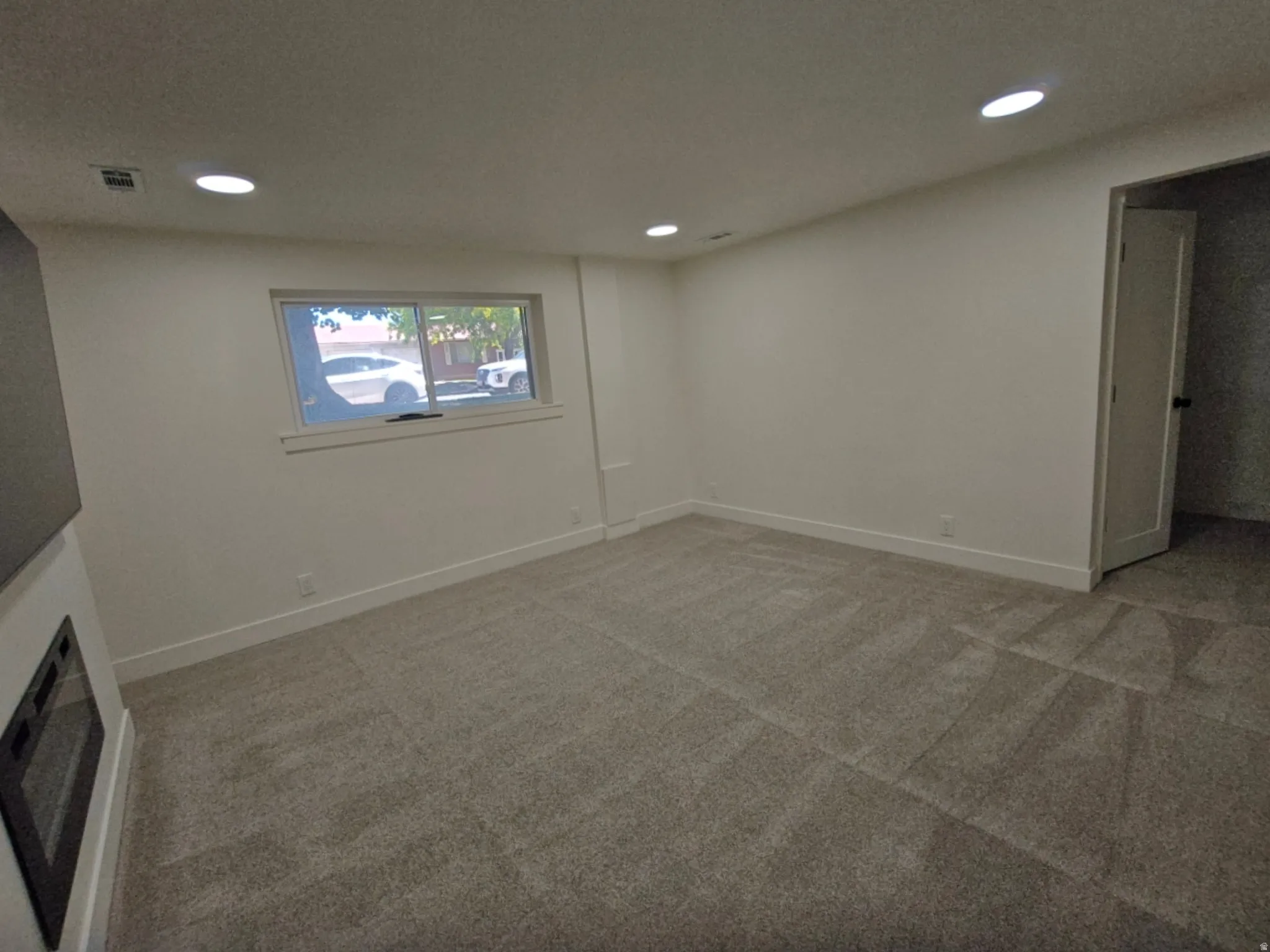 Spacious room featuring neutral carpet, white walls, recessed lighting, and a modern built-in fireplace