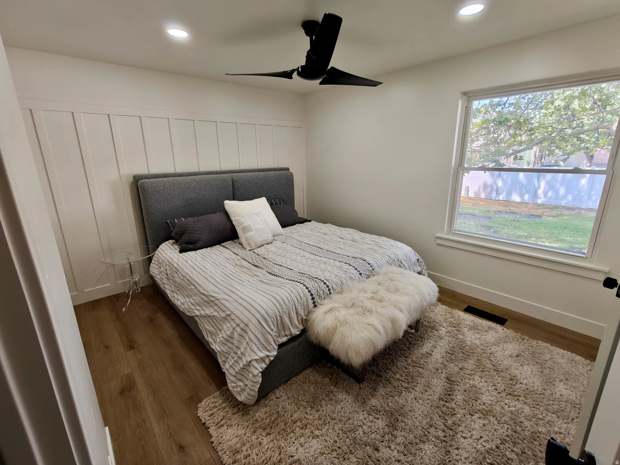 Bedroom featuring a board and batten accent wall, wood-finish flooring, a large window, recessed lighting, and a ceiling fan