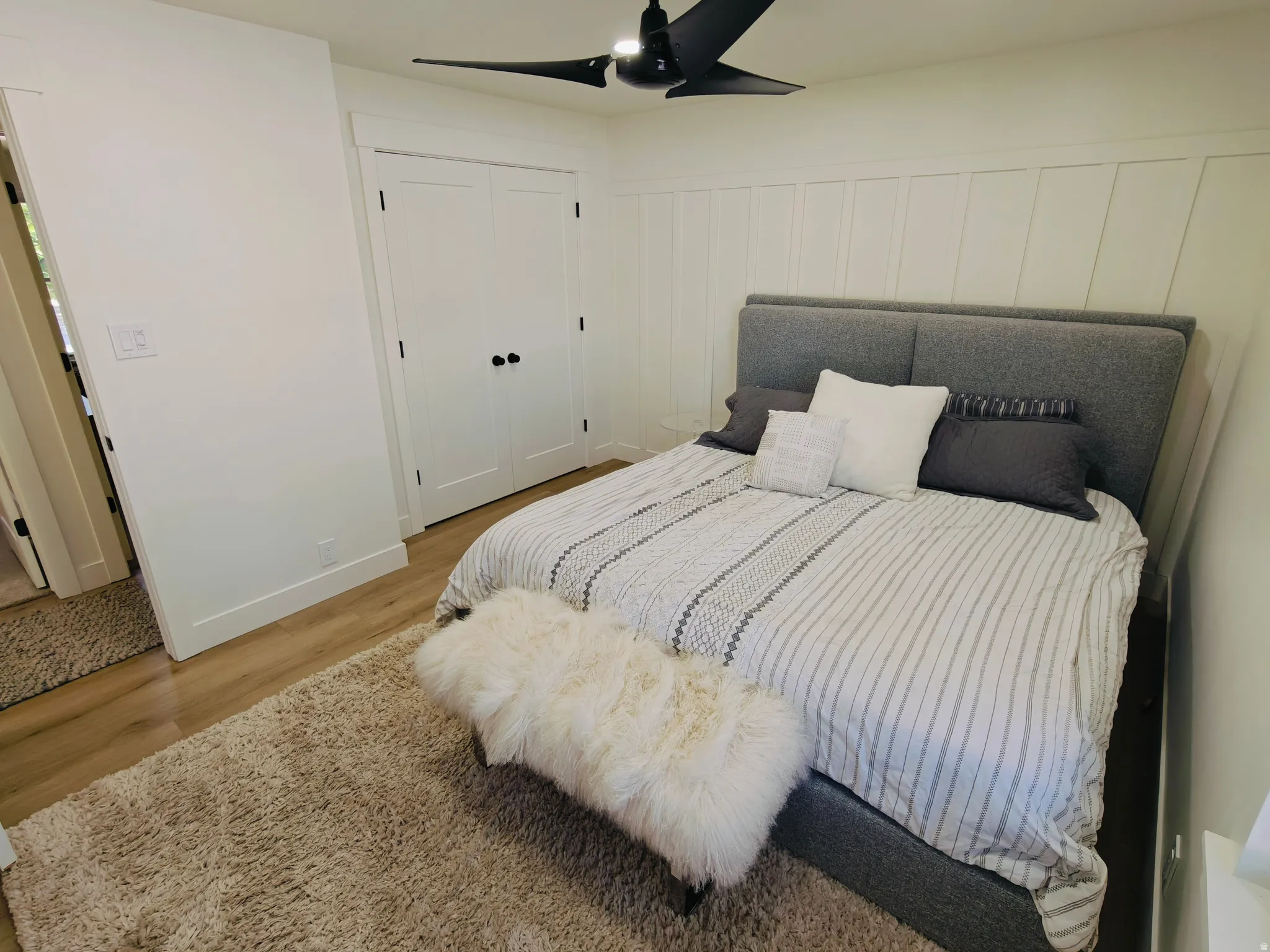 Bedroom featuring wood-finish flooring, a contemporary ceiling fan, and white paneled walls