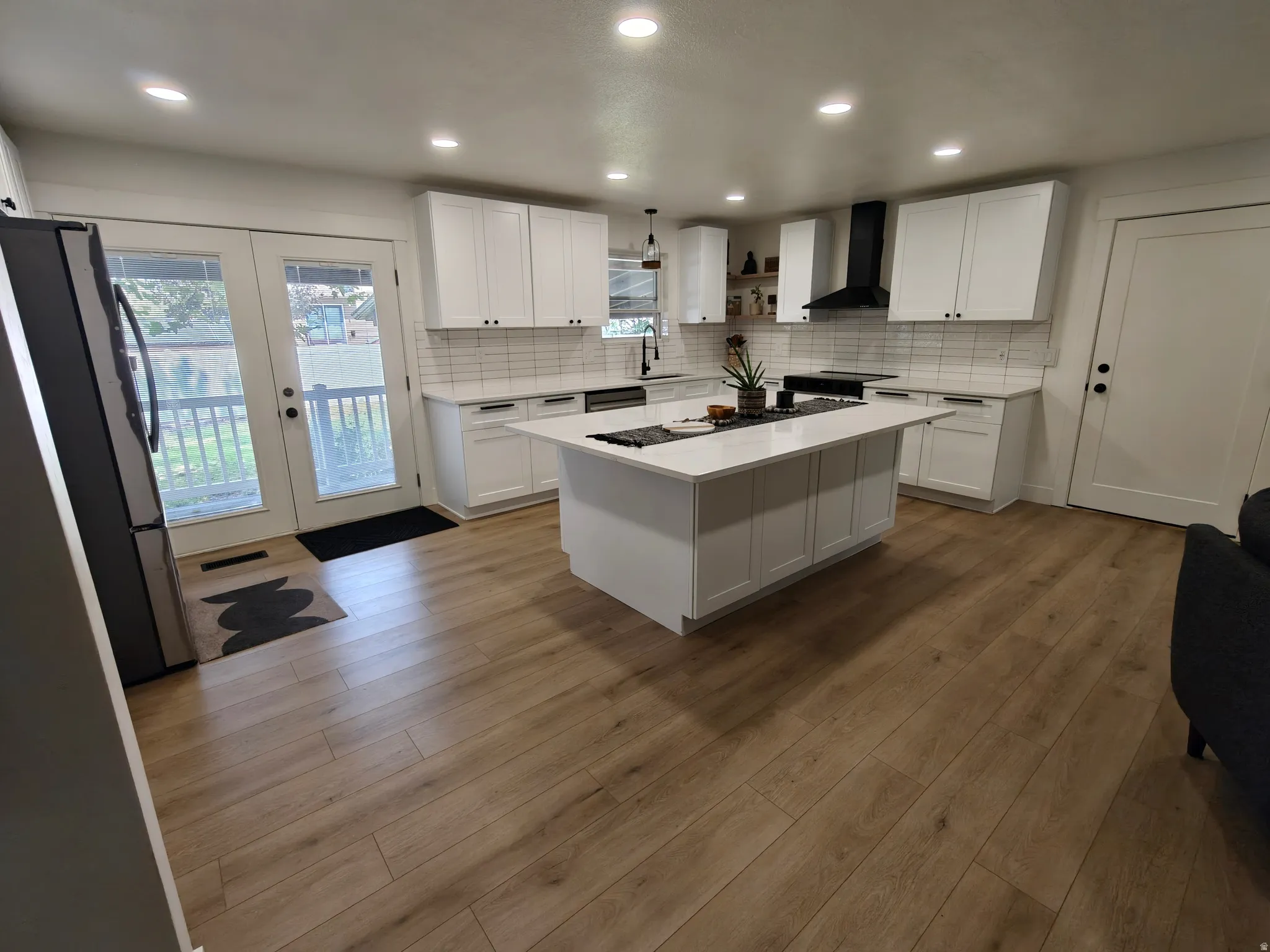 Open-concept kitchen with light wood-finish flooring, white cabinetry, a large kitchen island with a light-colored countertop, a white subway tile backsplash, and recessed lighting