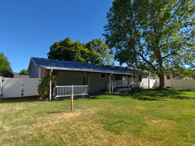 Spacious backyard with a large mature tree, featuring a covered patio and white vinyl fencing