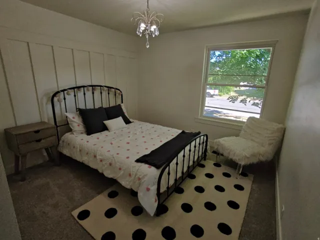Carpeted room featuring a white board and batten accent wall, a multi-pane window, and a decorative chandelier