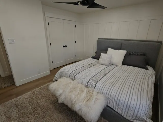 Bedroom with neutral-toned wood-finish flooring, white baseboards, and a contemporary ceiling fan