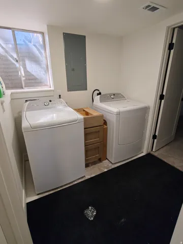 Dedicated laundry area featuring a utility sink cabinet, an electrical panel, and a basement window