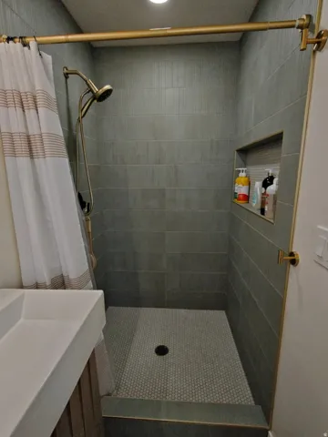 Walk-in shower featuring vertically stacked gray rectangular tiles and a hexagonal mosaic floor