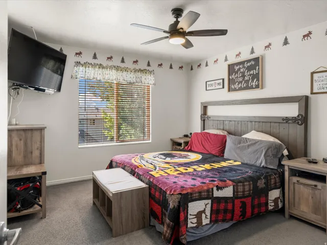 Carpeted room featuring a ceiling fan with integrated lighting, a window with horizontal blinds, and a mounted television