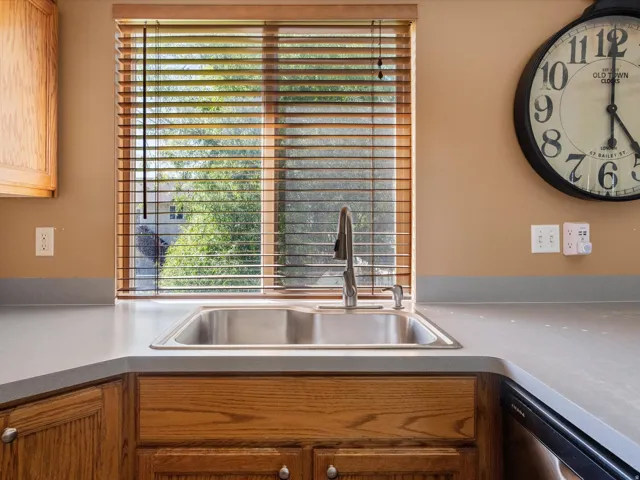 Kitchen sink featuring a stainless steel basin with a gooseneck faucet, light gray countertops, and wood-finish cabinetry