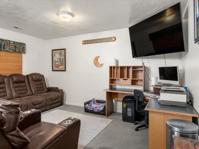 Carpeted room with a ceiling-mounted light fixture, wall-mounted television, and a window with blinds