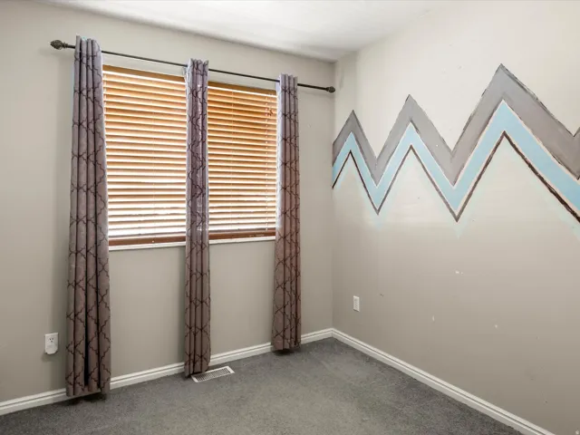 Room featuring window with wood blinds, patterned curtains, gray carpet, white baseboards, and a decorative wall accent