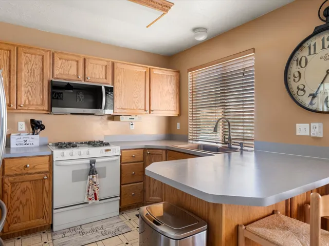 Kitchen featuring wood cabinetry, light-toned countertops, and a full suite of appliances including an oven/range and an over-the-range microwave