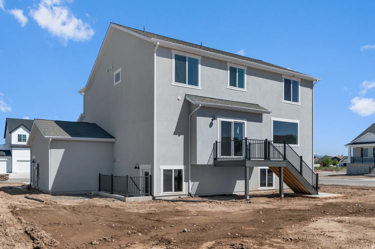 Contemporary stucco exterior featuring a second-story deck with dark railings, a sliding glass door, and multiple windows