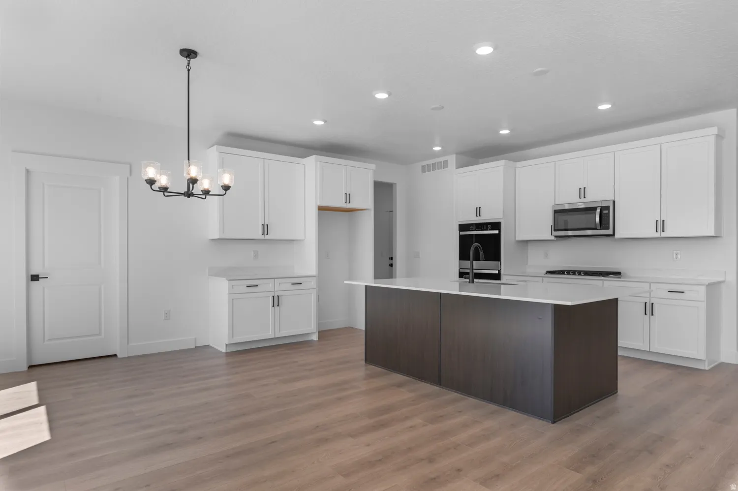 Open-concept kitchen with a dark wood-finish island, white cabinetry, integrated stainless steel appliances, and wood-finish flooring