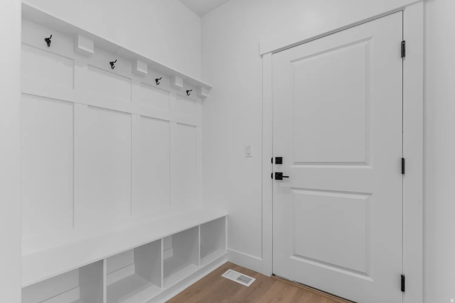 Entryway featuring a white built-in bench with integrated storage cubbies, white wall paneling with black coat hooks, and a white paneled door with matte black hardware