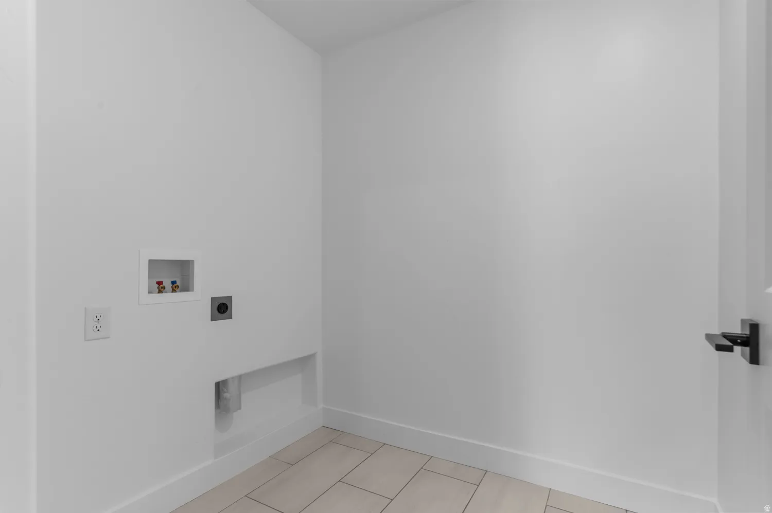 Dedicated laundry area featuring light-toned tile flooring, white walls, and a contemporary black door handle