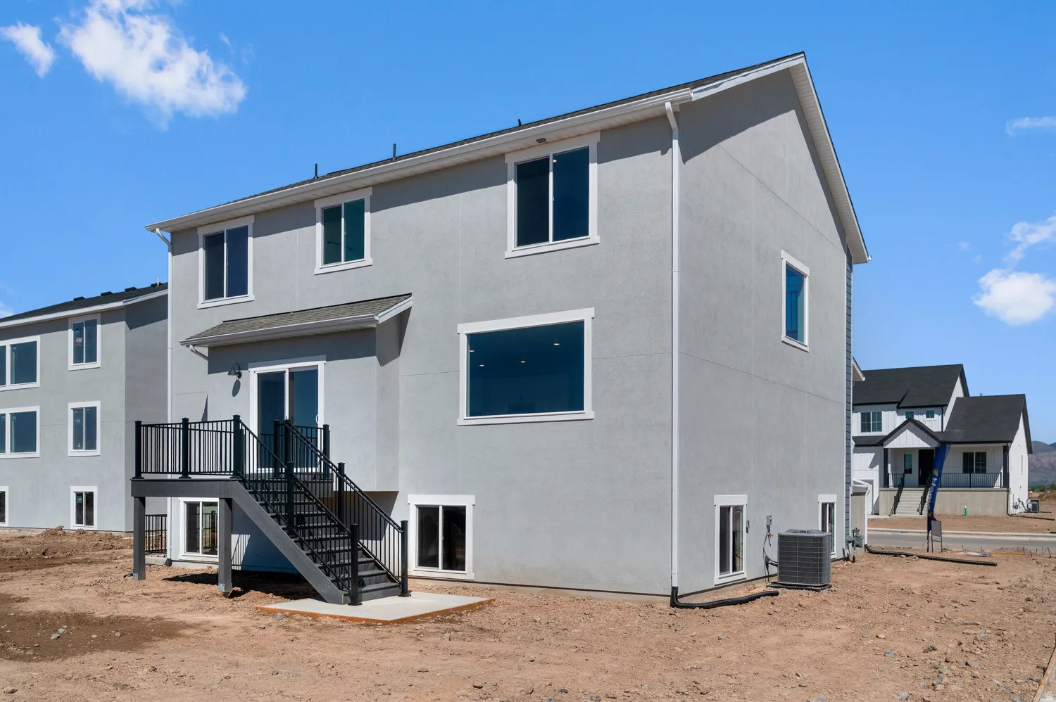 Gray stucco exterior with multiple windows, a rear deck with black railings, and a sliding glass door