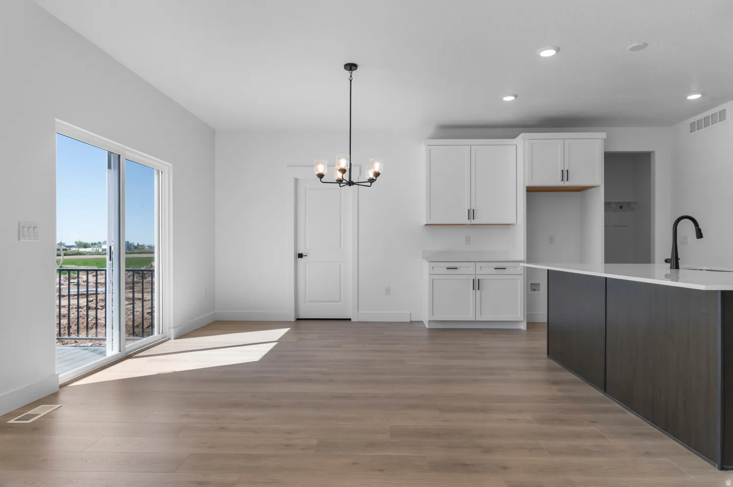 Contemporary open-concept space featuring wood-finish flooring, white walls, and a sliding glass door leading to a balcony with black railings